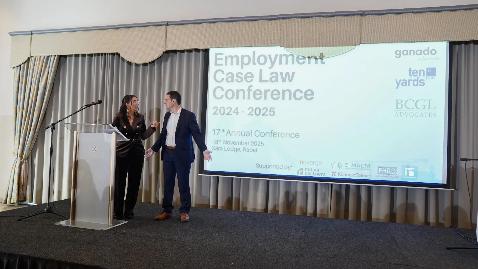 Two presenters on stage beside the 17th edition conference screen
